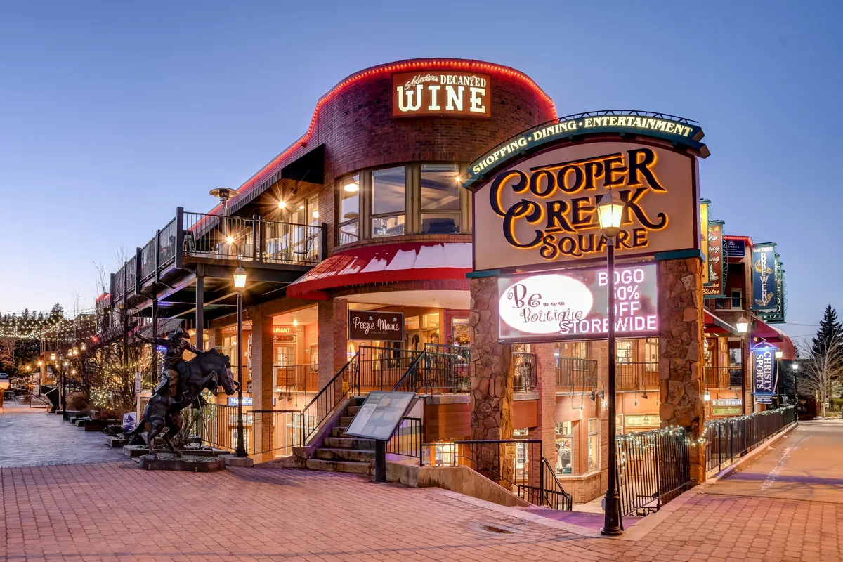 A lively street scene in downtown Winter Park featuring the Cooper Creek Square sign, wine shop, outdoor seating, and a horse statue. The area bustles with opportunities for shopping, dining, and group outings.