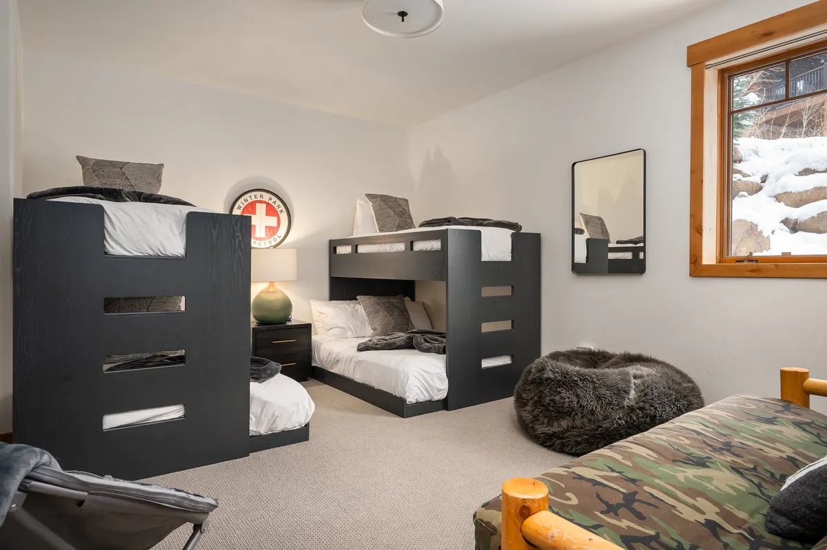 A playful bunk room with twin-over-full bunk beds, a bean bag chair, a window with a view, and a green lamp. The room is designed for comfort and fun, making it highly appealing to kids and teens.