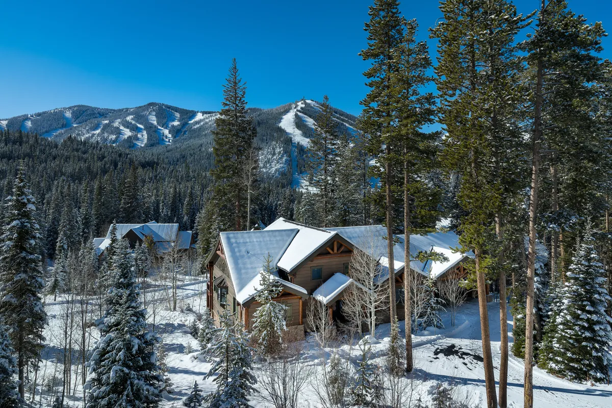 A luxurious log cabin nestled among snow-covered trees with a dramatic mountain backdrop. The cabin glows warmly against the tranquil, snowy landscape, evoking a sense of exclusivity and connection to nature. The scene captures the essence of a winter retreat, highlighting opportunities for both adventure (skiing, hiking) and cozy relaxation.