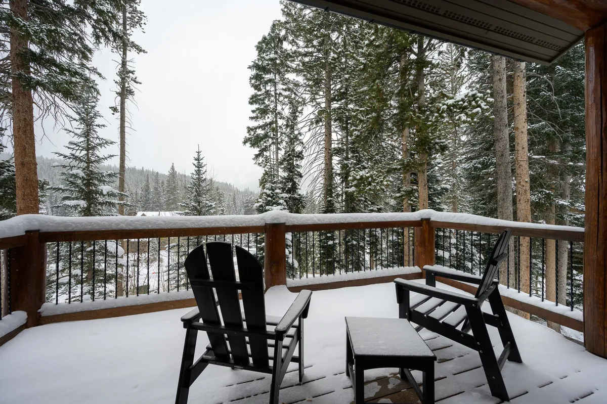 A tranquil wooden deck with snow-covered chairs, bordered by trees, offering a peaceful spot for conversation or reflection. The setting is ideal for enjoying nature, sipping hot cocoa, or stargazing on clear nights.