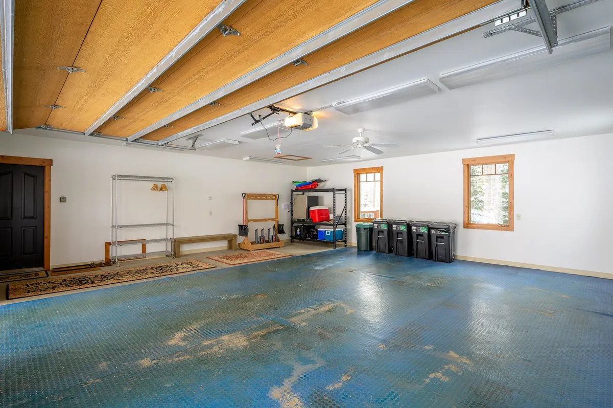 A spacious, well-organized garage with ample shelving, large windows, and clean floor space. The room is practical and tidy, ideal for storing skis, snowboards, or summer gear.