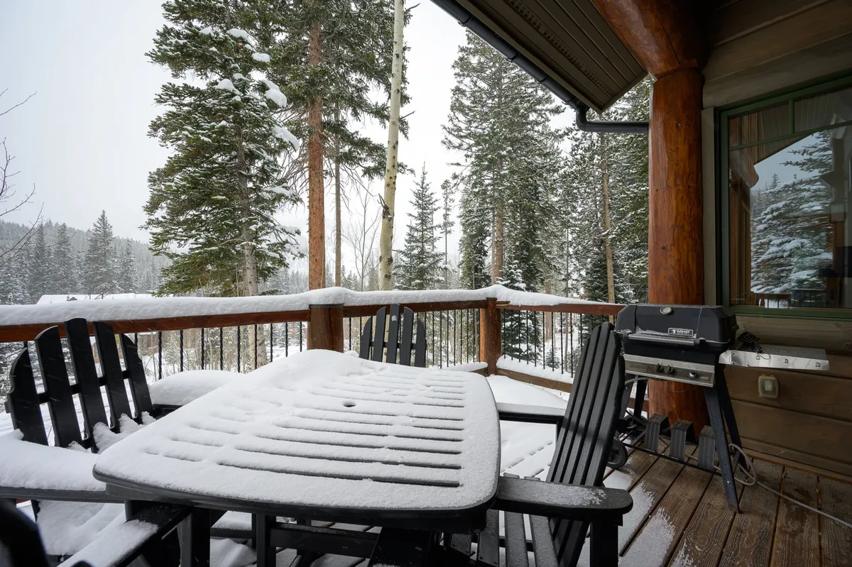 An inviting outdoor deck scene with a snow-covered table, sleek black chairs, and a grill, set against a backdrop of wintry trees. This deck area is ideal for al fresco drinks, grilling, or simply soaking up the Colorado scenery in any season.