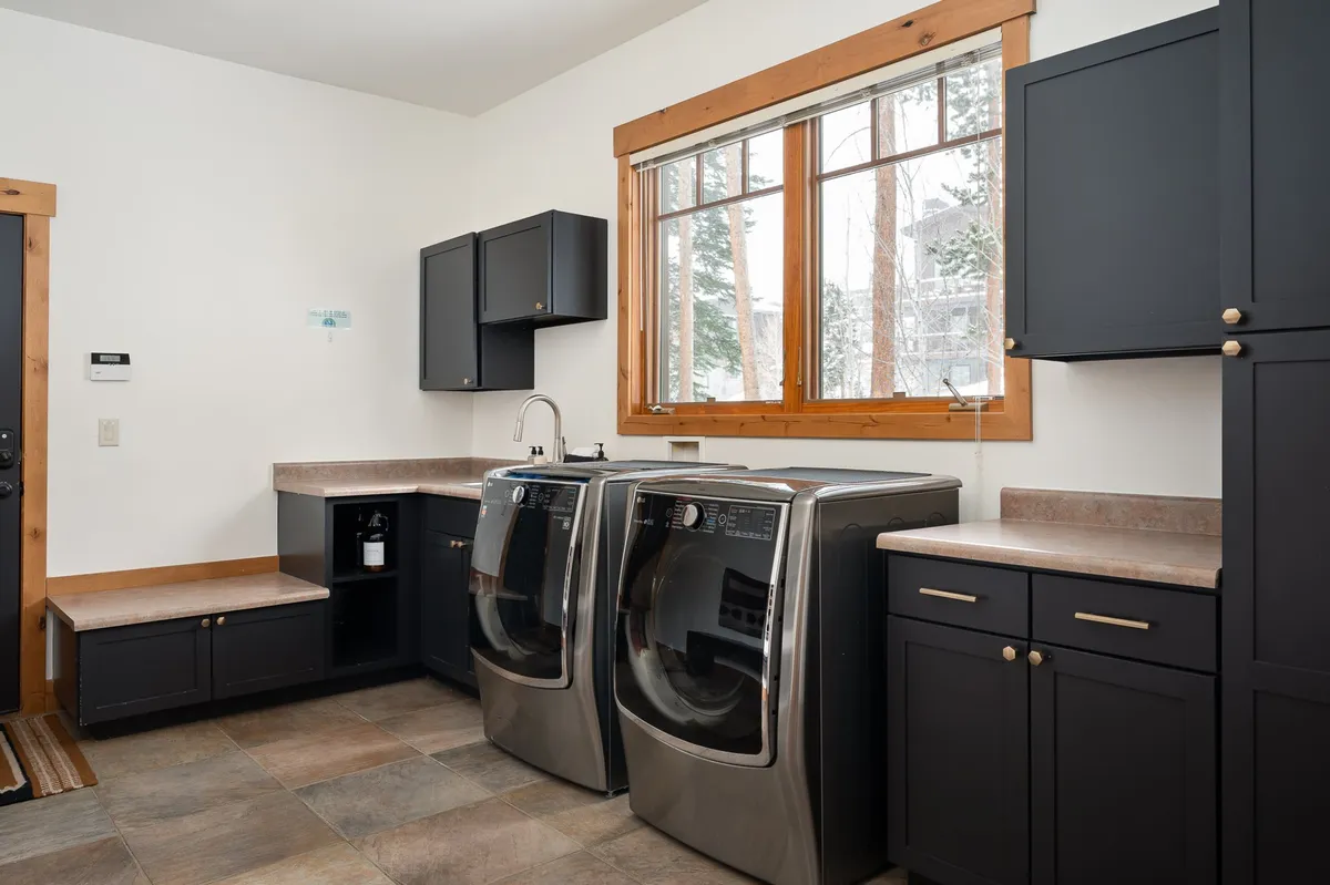 A practical and organized laundry room with modern washing machines, a window that lets in natural light, and a clean counter space for sorting clothes or prepping gear. The environment feels functional yet welcoming, supporting the theme of convenience for adventure-oriented guests.