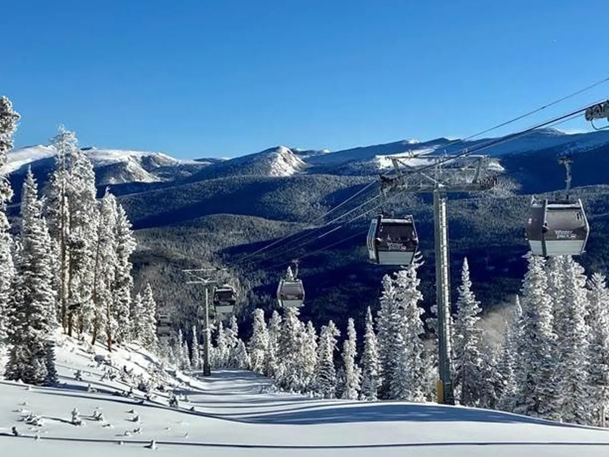 This image showcases an expansive mountain landscape with ski lifts crossing snow-covered slopes, surrounded by snow-laden evergreens and a dramatic mountain range in the background. The scene buzzes with activity from skiers and snowboarders and radiates the excitement of the winter sports season.