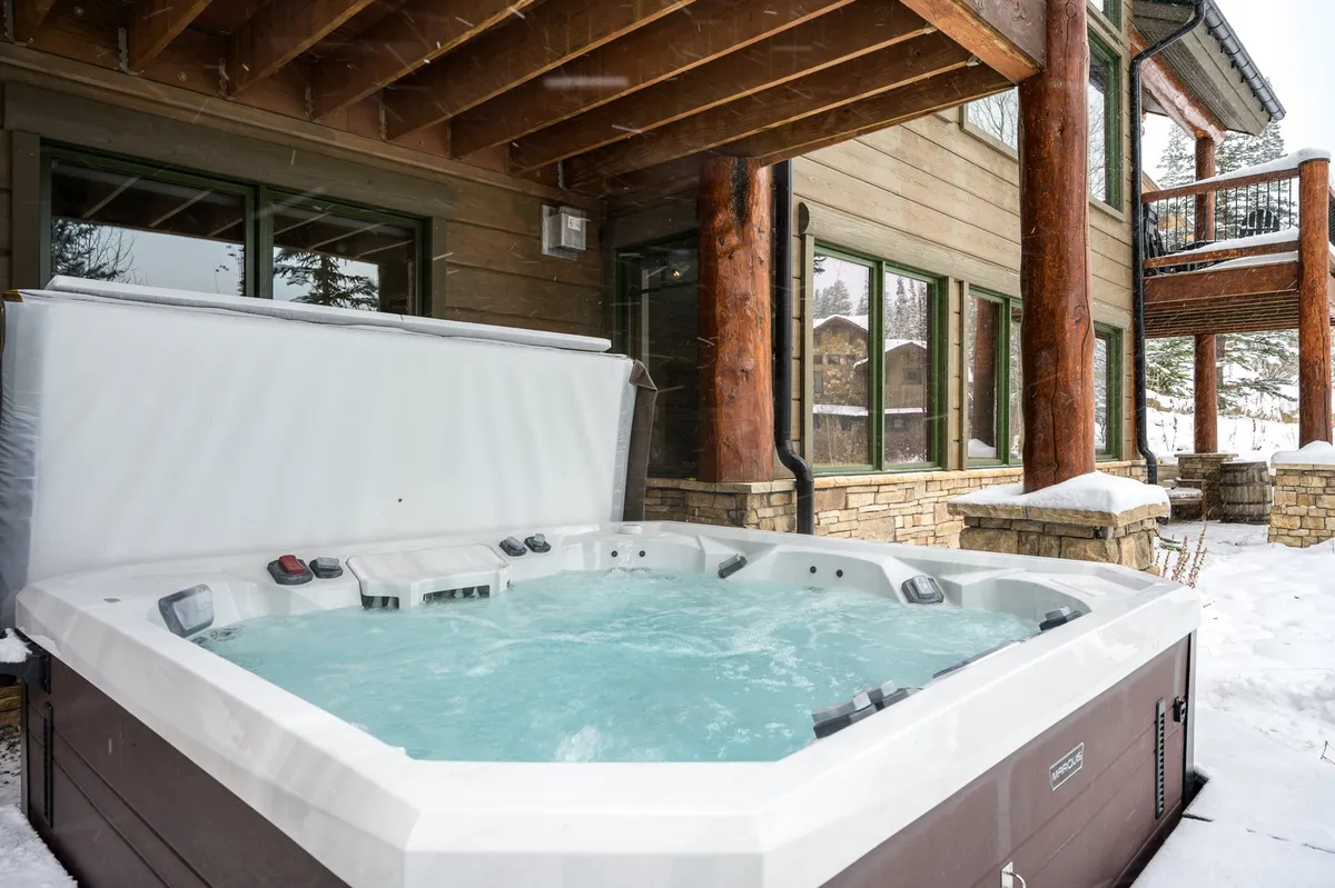 An outdoor hot tub set against a snowy landscape, framed by wooden beams and a stone exterior. The bubbling water and surrounding snow create a serene, luxurious atmosphere ideal for relaxation after outdoor adventures.