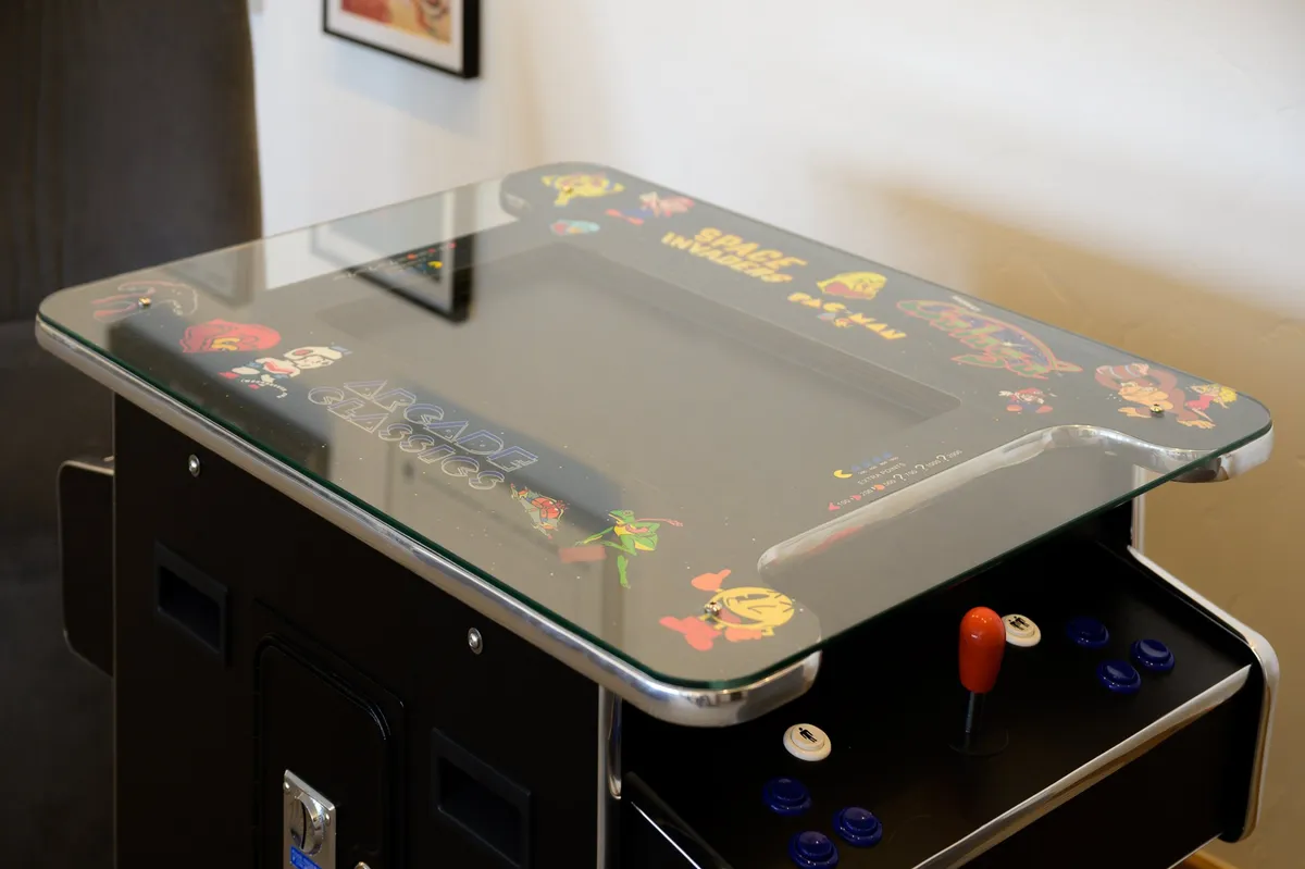 A close-up of a classic arcade game machine with colorful graphics and a control panel, set in a dedicated recreation space. The mood is nostalgic and playful, inviting friendly competition and shared laughter.