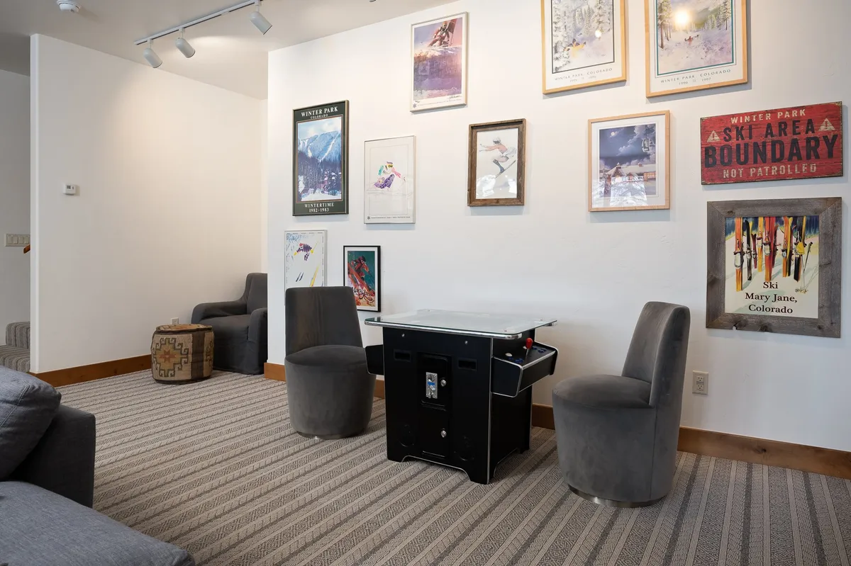 A cozy game room with a game table, comfortable seating, and artwork on the walls. The space is designed for social gatherings and relaxation, with warm lighting and ski-themed decor that nods to mountain adventures.