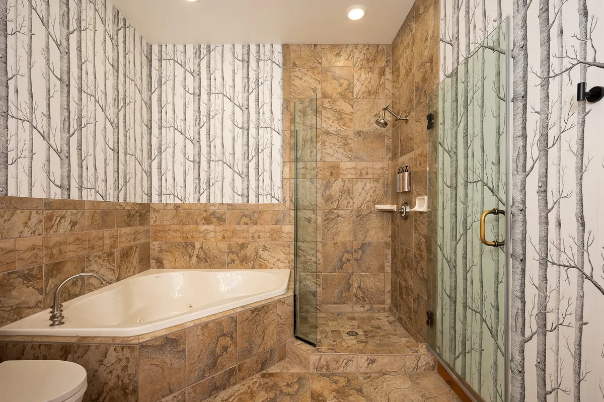 A spa-like bathroom with a freestanding soaking tub, glass shower enclosure, and tree-patterned wallpaper. The overall look is tranquil and rejuvenating, offering a luxurious setting for relaxation and self-care.